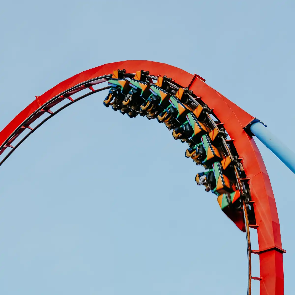 A red roller coaster arching across a blue sky